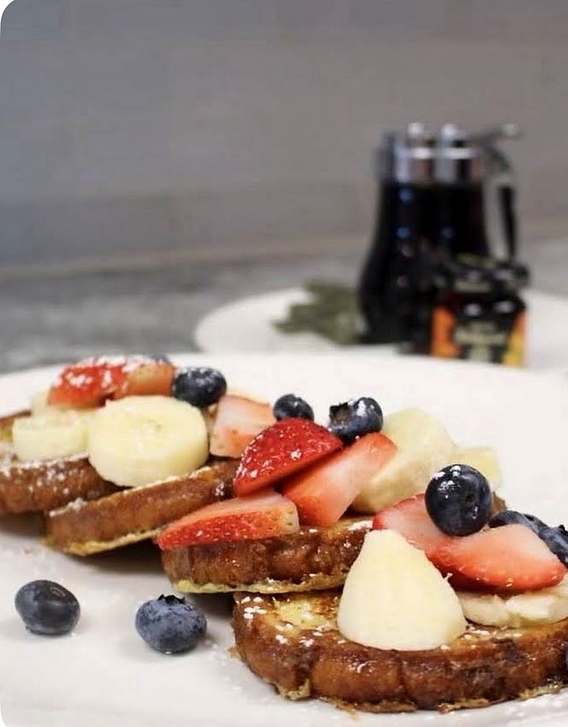 French toast topped with strawberries, blueberries and bananas with syrup