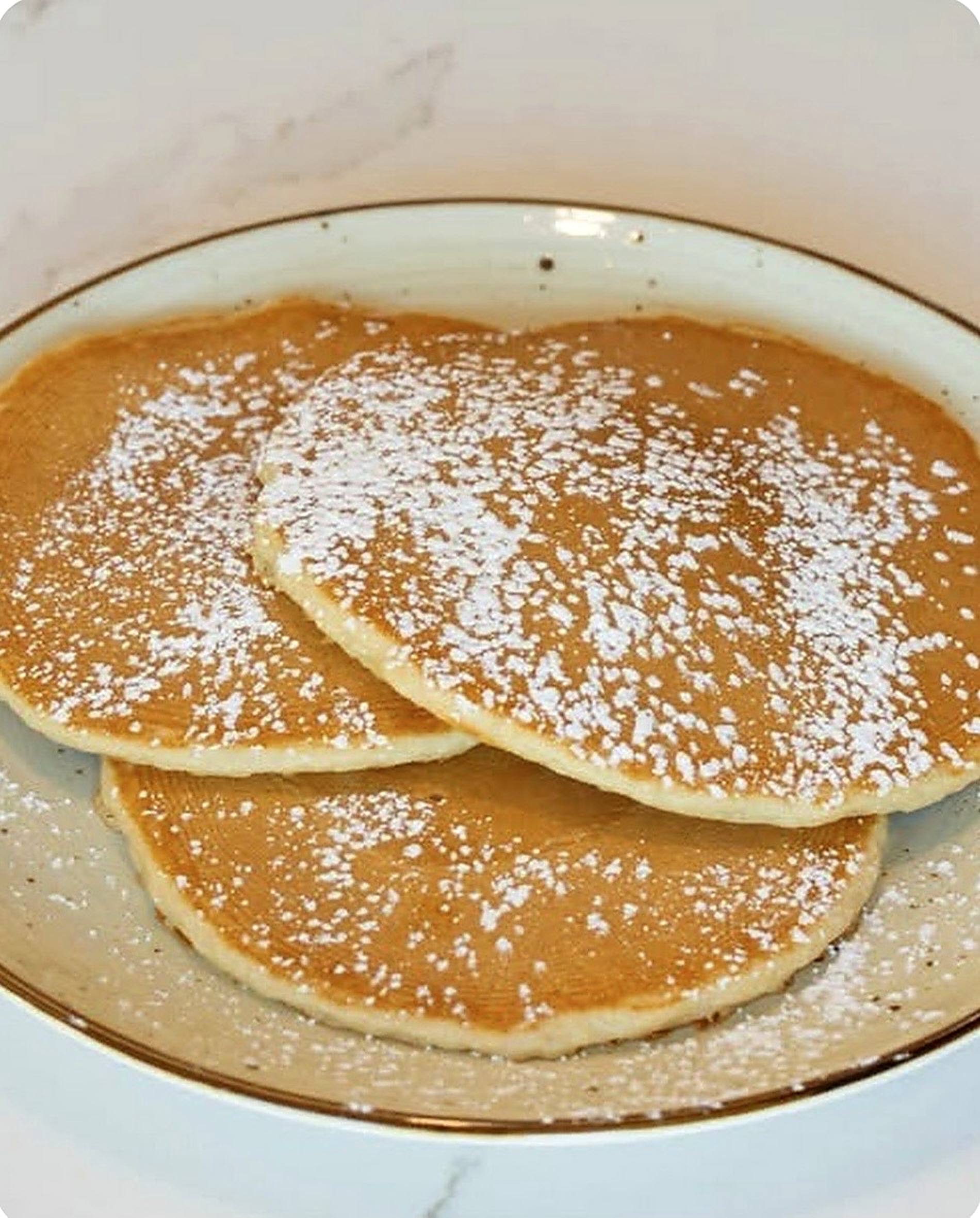 Three buttermilk pancakes dusted with powdered sugar