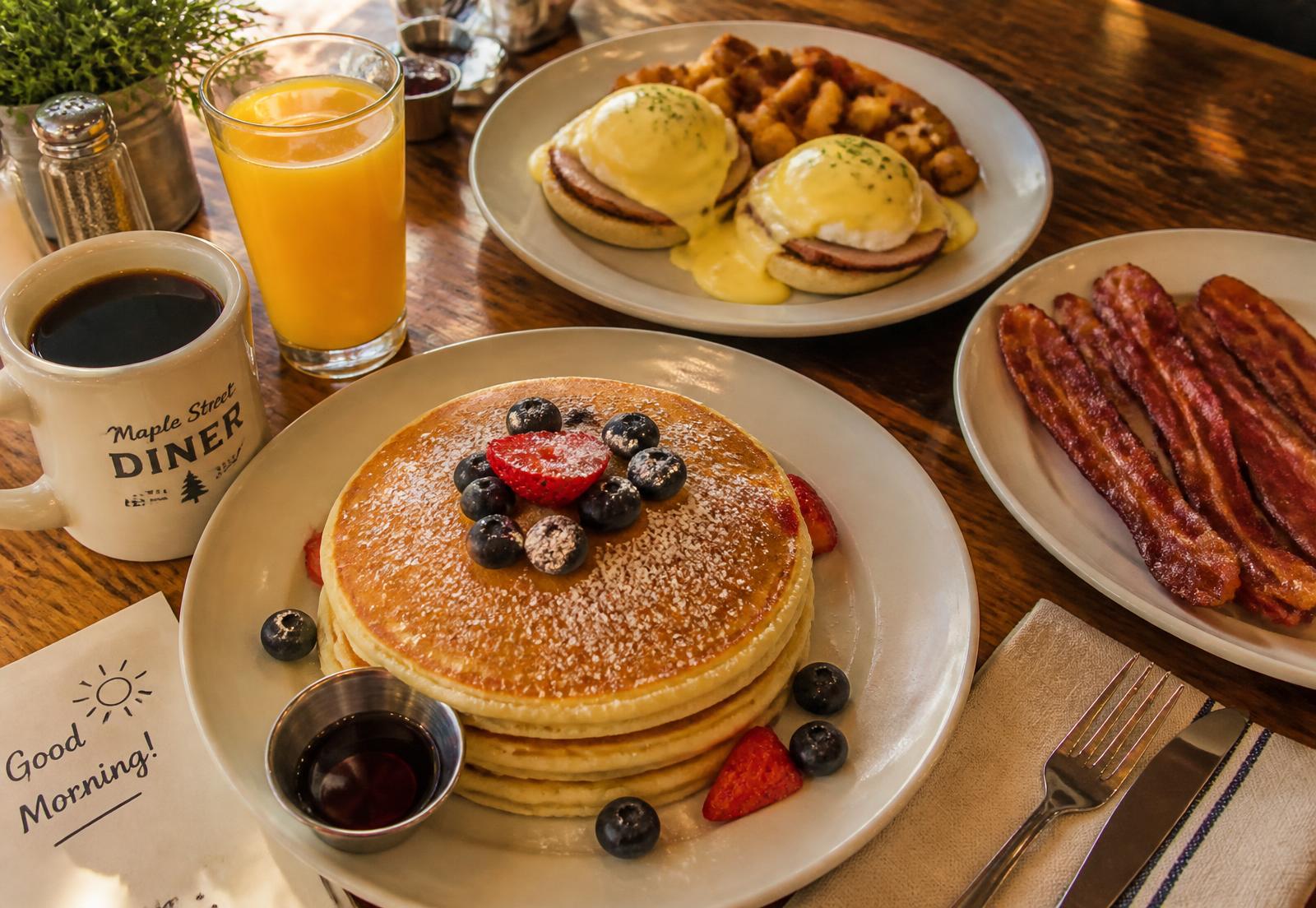 Pancakes, eggs benedict, bacon and coffee on a wooden table